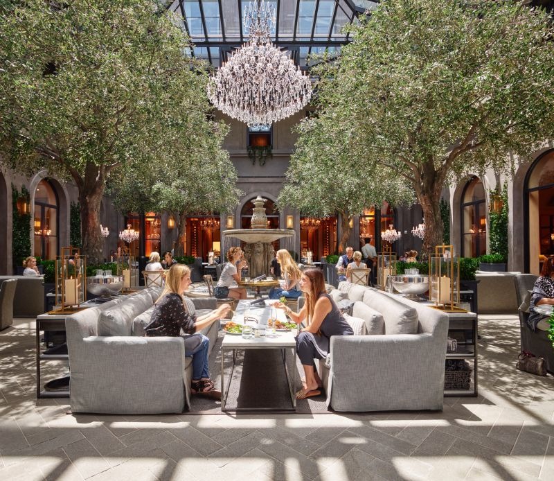 Espacio exterior resguardado del restaurante con vegetación, mesas y entrada de luz diurna